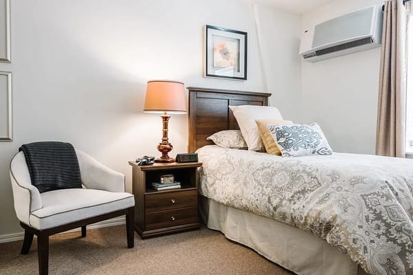 A cozy bedroom featuring a bed, nightstand with lamp, and seating area.