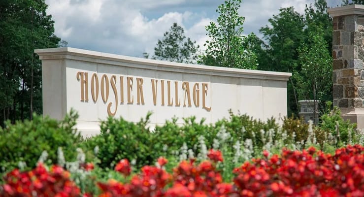 Sign of Hoosier Village surrounded by flowers and greenery