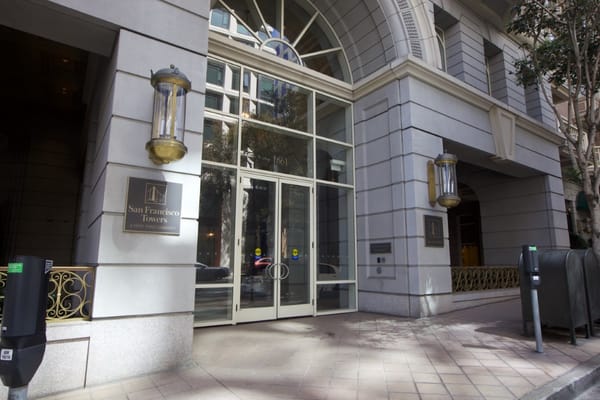 Front entrance of San Francisco Towers with glass doors and sign.