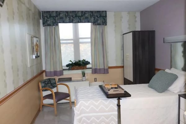 Cozy room featuring a bed, chair, and window with curtains.