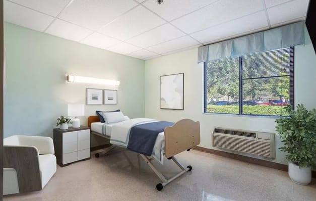 A well-furnished bedroom with a bed, chair, and window at Indian River Center.