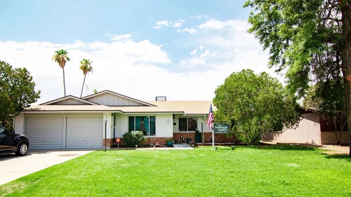 Exterior view of an assisted living facility with a lawn and palm trees