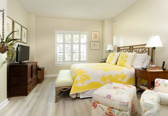 A comfortable bedroom featuring a yellow quilt, decorative furniture, and a TV.