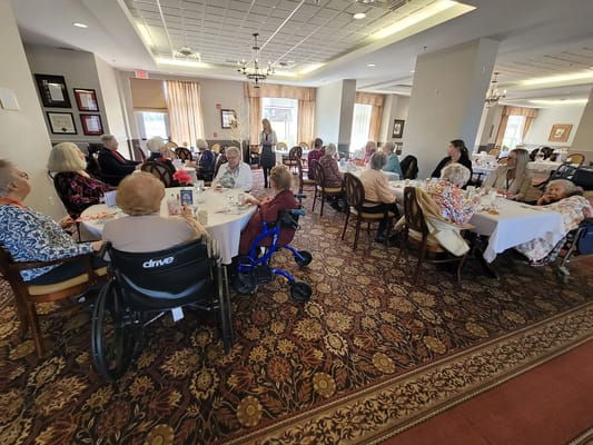 Seniors gathered around tables in a dining room enjoying a meal.