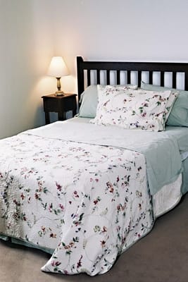 A nicely arranged bedroom with floral bedding and a bedside lamp.
