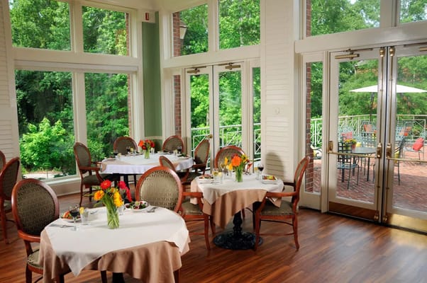Dining room with tables, flowers, and large windows overlooking greenery