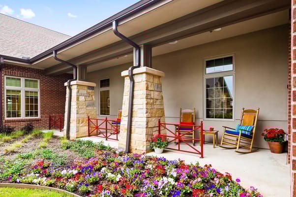 A serene patio area with rocking chairs and a vibrant flower bed.