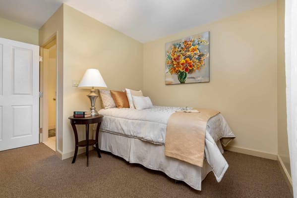 A cozy bedroom featuring a bed with decorative pillows and a floral painting.