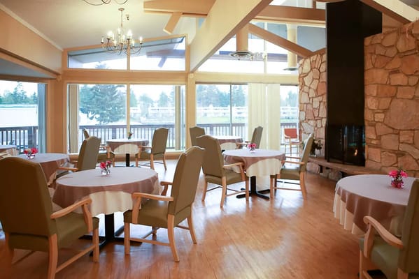 Cozy dining area with tables and chairs, featuring large windows and a stone fireplace.