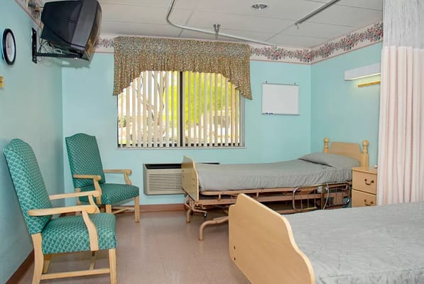 A shared senior living room with two beds and green chairs.