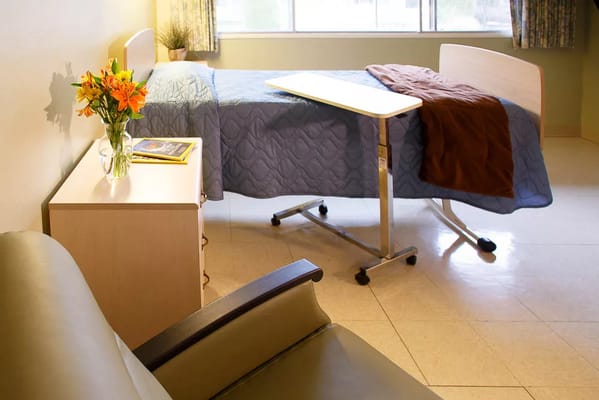 A resident room featuring a bed, a chair, and a vase of flowers