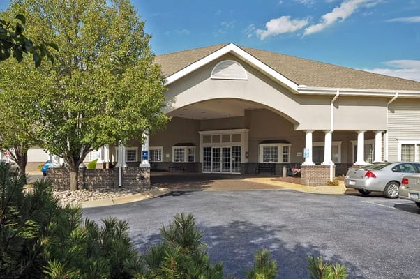 Front entrance of Life Care Center of Wichita with greenery and parked cars.