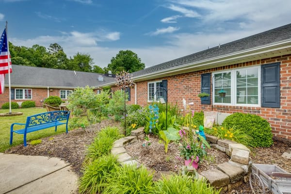 Flowerbed and blue bench in front of a senior living facility.