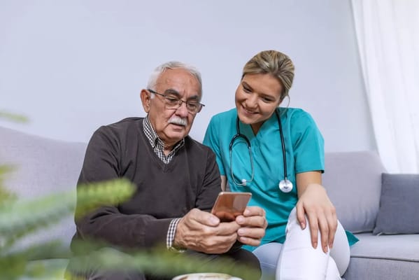 A nurse assisting an elderly man with his phone