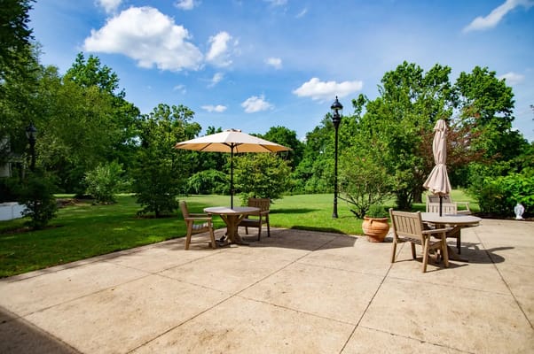 Patio with tables, chairs, and an umbrella in a garden setting