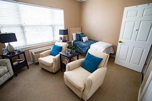 Comfortable bedroom featuring two armchairs, a bed, and window blinds.