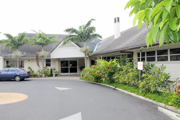 Entrance view of Maunalani Nursing and Rehabilitation Center with lush greenery and a parking area.