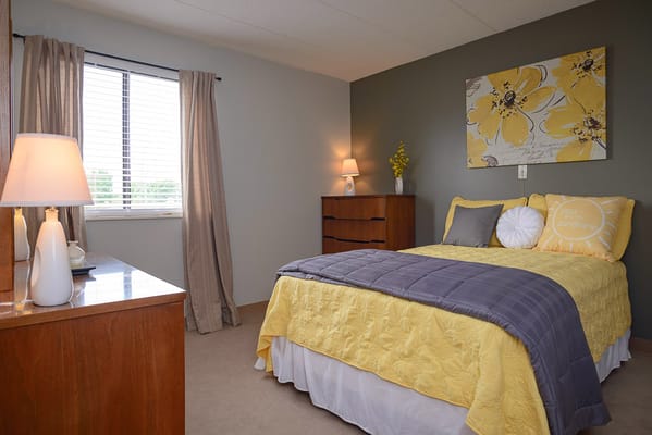 A bright bedroom with yellow accents, featuring a bed, dresser, and window.