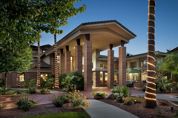 The entrance of McDowell Village illuminated at dusk, showcasing lush landscaping and palm trees.
