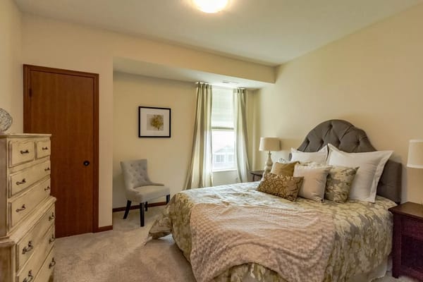 Cozy bedroom with a bed, dresser, and chair in Mill Pond facility.