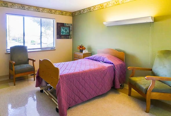 A bright bedroom with a single bed, two chairs, and a window.