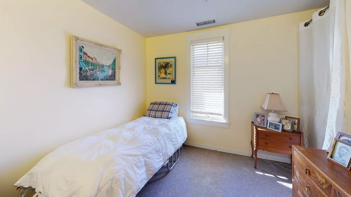 A well-lit bedroom with a single bed, artwork on the walls, and a bedside table.