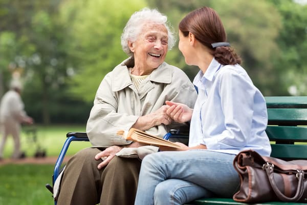Elderly woman laughing with caregiver in a park