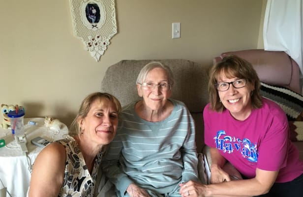 Three women smiling together in a cozy living room area.