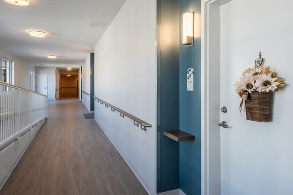 A well-lit hallway featuring room numbers and a decorative flower arrangement.