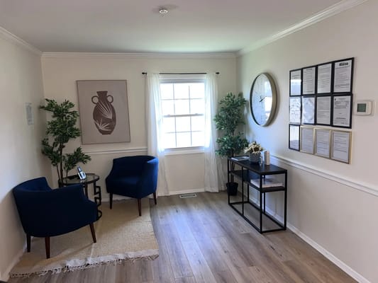 A cozy lobby featuring two blue chairs, a small table, and decorative plants.