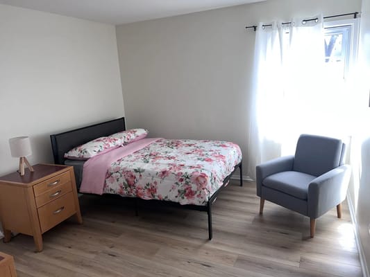 A cozy bedroom with a floral bedspread, bedside table, and armchair