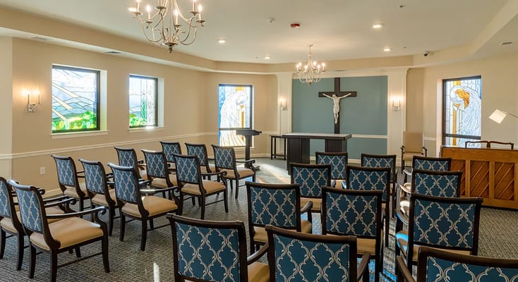 Brightly lit interior chapel with rows of chairs and stained glass windows.