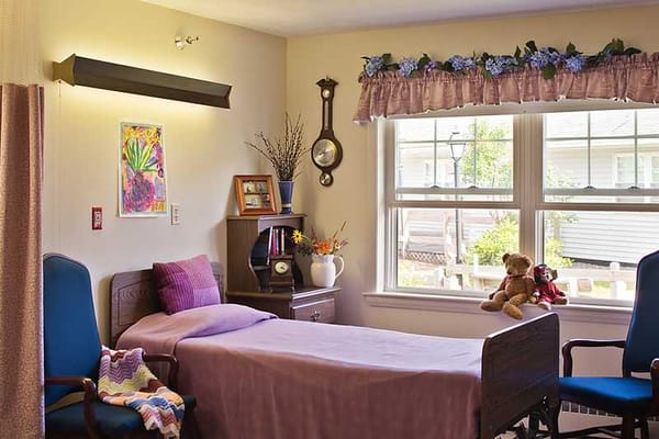 A furnished bedroom in Orono Commons featuring a bed, blue chairs, and a window.