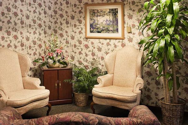 A cozy living room space with two upholstered chairs, a plant, and floral wallpaper.