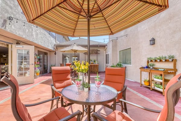 Outdoor patio with orange chairs, a table, and a flower arrangement under a striped umbrella.