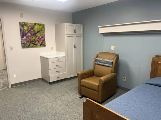 A well-furnished resident room with a chair, bed, and storage in Papillion Manor.