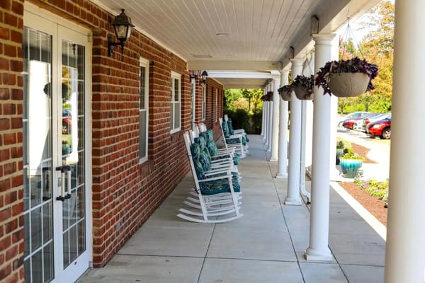 Rocking chairs lined up on a porch next to a brick building
