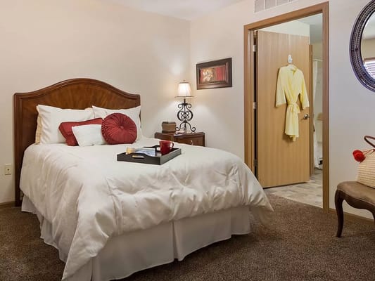 A cozy bedroom with a bed, lamp, and door leading to a bathroom