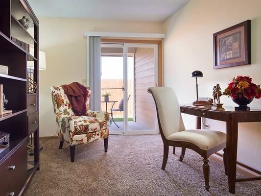 A cozy living room setup with an armchair, desk, and sliding door to a patio.