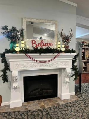 Decorated mantel with 'Believe' sign and festive greenery.