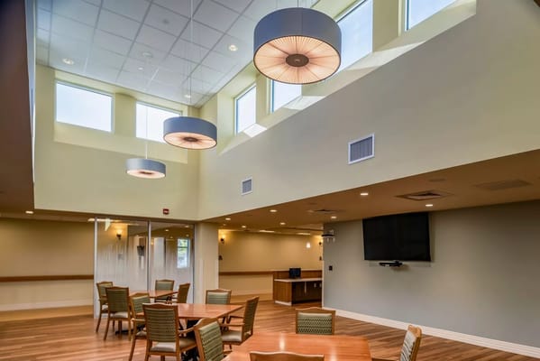 Bright common area featuring tables, chairs, and large windows.