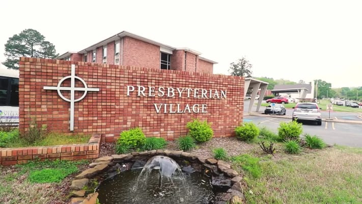 Sign of Presbyterian Village with a fountain and greenery