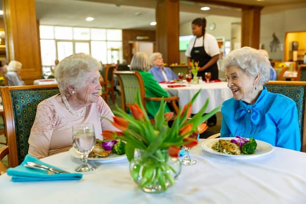 Two senior women laughing over a meal at a dining table