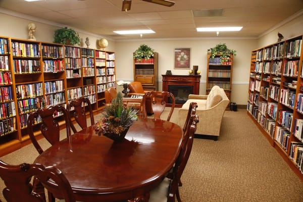 Interior view of a library with bookshelves, seating area, and a dining table