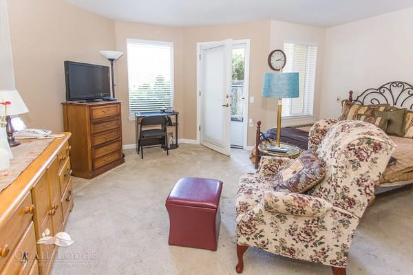 A cozy bedroom featuring a dresser, television, and floral armchair