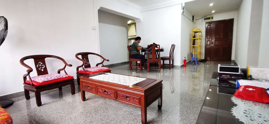 A living room with traditional wooden furniture and a person seated at a dining table.