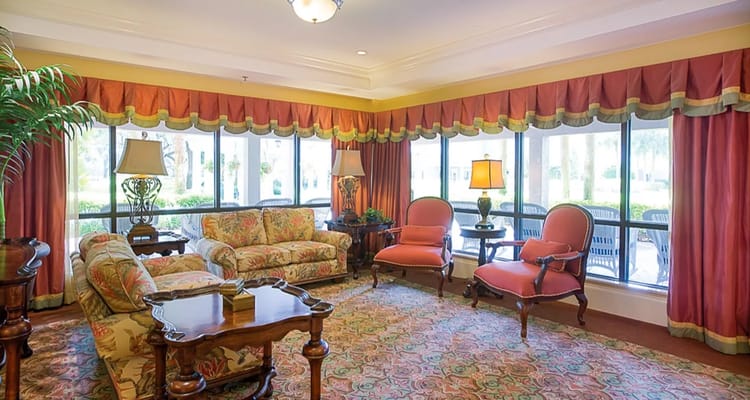 A comfortable living room with floral sofas, lamps, and large windows.