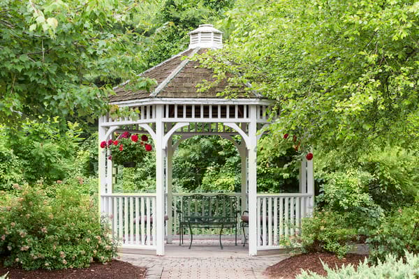White gazebo surrounded by green foliage and flowers