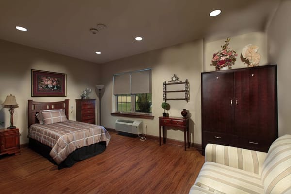 A cozy bedroom featuring a bed, dresser, and seating area.