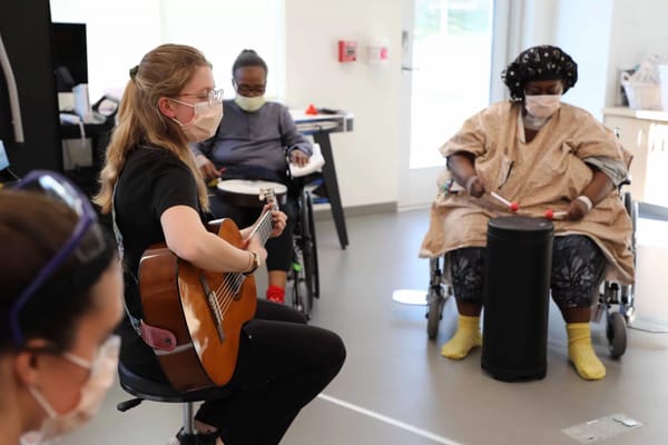 Residents participating in a music therapy session with a guitarist and drummer.